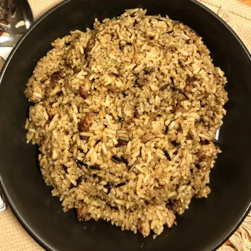 wild rice and sausage stuffing plated in black bowl on tan fabric over wooden cutting board