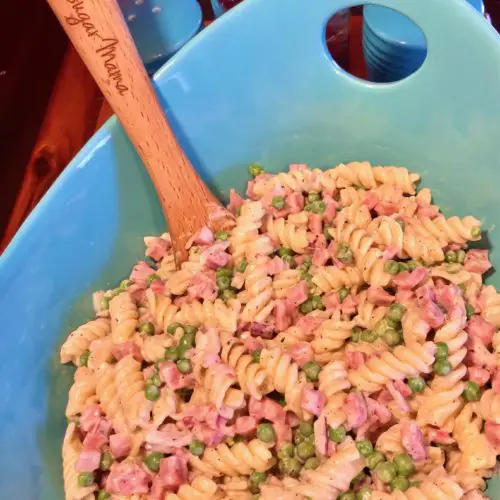 bacon ranch ham pasta salad in light blue serving bowl with wooden spoon. Rotini pasta with sweet peas, purple onion and diced ham