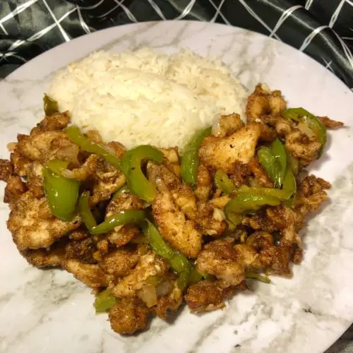 Chinese pepper chicken served with jasmine rice. plated on white and gray marble plate with dark gray marbled cutting board and black and white napkin in the background