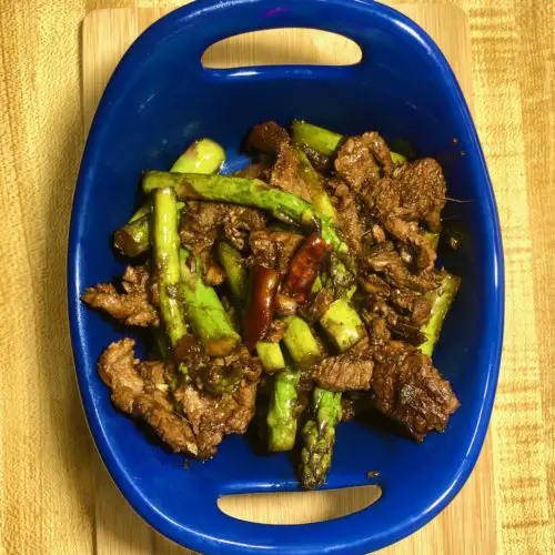 steak and asparagus stirfry with thai chili pepper plated in royal blue bowl on oak counter