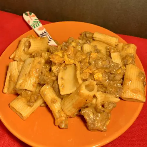 cheesy taco rigatoni with ground beef plated on orange plate with floral fork on red fabric