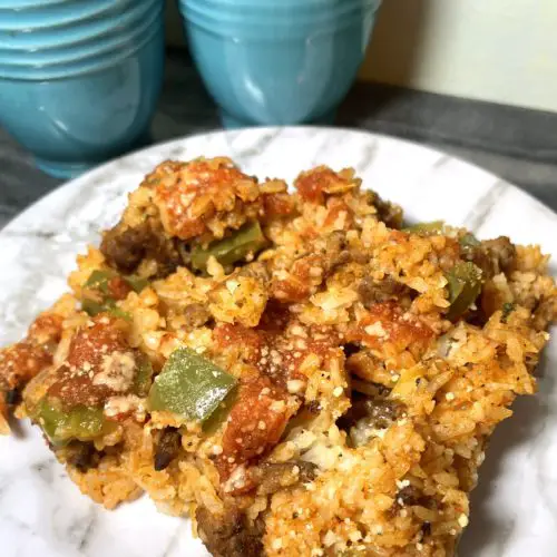 Unstuffed pepper rice casserole on a white marbled plate onto of a gray marble cutting board and pictured with large bright blue salt and pepper shakers in the background.