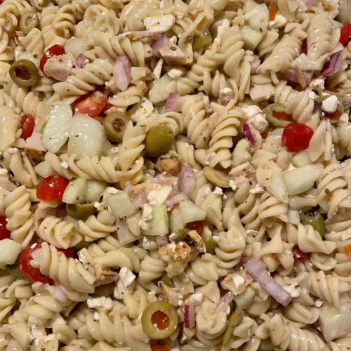 Greek pasta salad with grilled chicken pictured overhead in a foil tray.