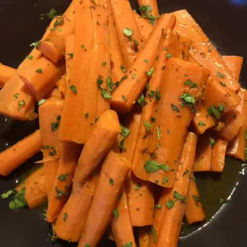 Orange Apricot Glazed Carrots pictured in a black bowl and garnished with fresh parsley.